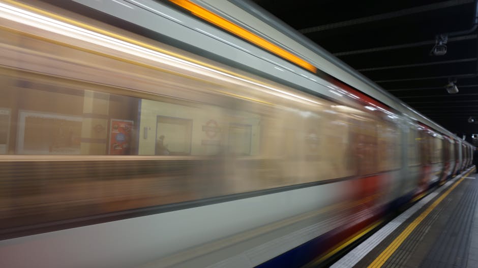 View through an oval-shaped window of a modern underground station platform featuring wooden panelled walls with a warm, natural wood finish. The platform has a smooth, light grey floor with a tactile